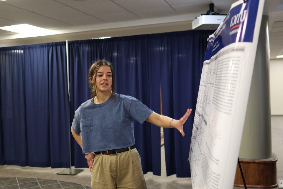 A student makes a presentation beside a poster at the 2024 Student Conference for 研究, Professional Activities, 及创意艺术