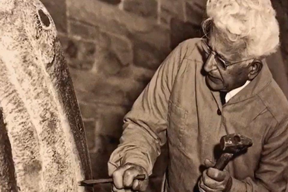 亨利·迪斯皮里托(Henry Dispirito)在雕塑上工作的黑白照片，手里拿着锤子和凿子.